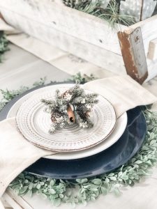 An easy winter table setting with navy chargers, white dishes and greenery